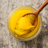Wooden spoon scooping ghee from glass jar on rustic table Clarified butter or ghee in open glass jar with wooden spoon on rustic wooden background